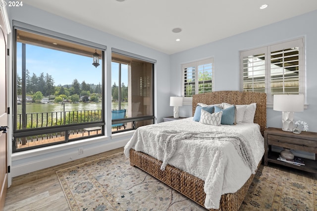bedroom featuring recessed lighting, a water view, wood finished floors, and baseboards