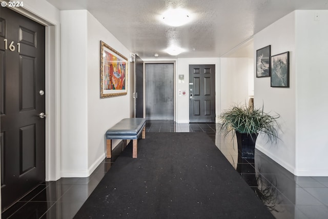 corridor with a textured ceiling, baseboards, and tile patterned floors