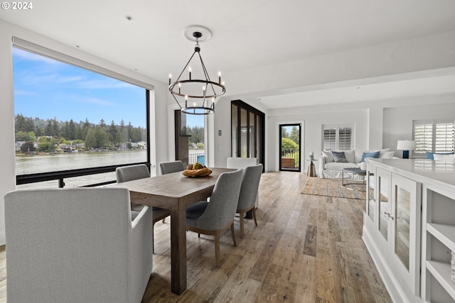 dining space with a healthy amount of sunlight, wood-type flooring, a water view, and a notable chandelier