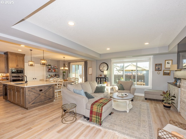 living room with an inviting chandelier, a raised ceiling, a wealth of natural light, and light hardwood / wood-style floors