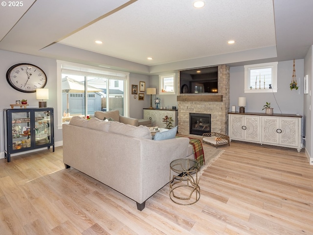 living room featuring a stone fireplace, light hardwood / wood-style flooring, and a raised ceiling