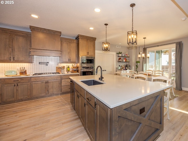 kitchen featuring stainless steel appliances, sink, a kitchen island with sink, and light wood-type flooring