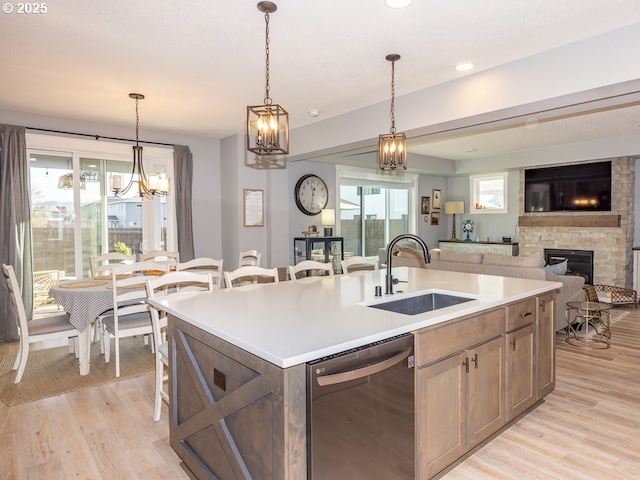 kitchen with a stone fireplace, sink, a center island with sink, light hardwood / wood-style flooring, and dishwasher