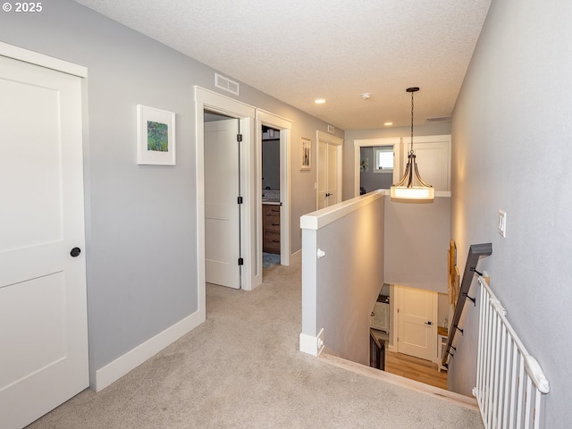 hallway with light colored carpet and a textured ceiling