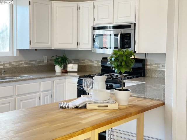 1035 NE Killingsworth St, Portland, OR 97211 - kitchen with stainless steel microwave, butcher block countertops, black gas range, white cabinetry, and tasteful backsplash