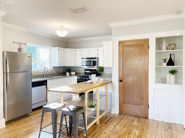 1035 NE Killingsworth St, Portland, OR 97211 - kitchen with appliances with stainless steel finishes, white cabinets, ornamental molding, and light wood-style flooring