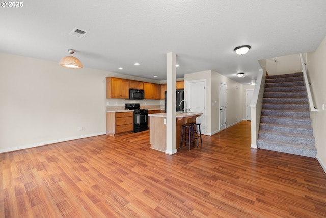 834 NW 3rd Ave, Canby, OR 97013 - kitchen with black appliances, light wood finished floors, a kitchen bar, light countertops, and brown cabinetry