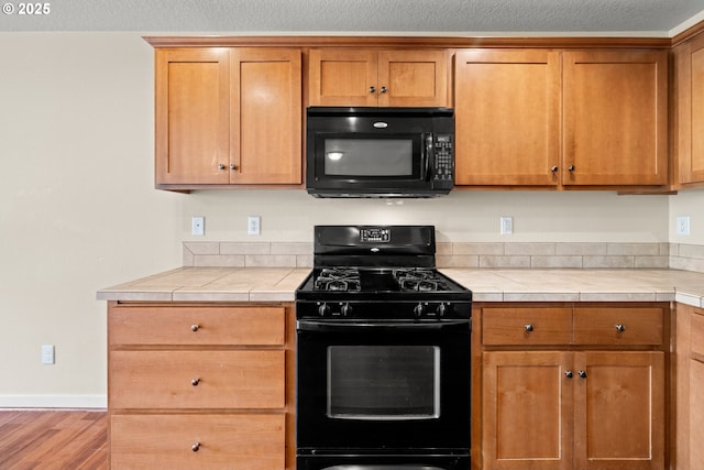 834 NW 3rd Ave, Canby, OR 97013 - kitchen featuring black appliances, tile countertops, wood finished floors, and brown cabinets