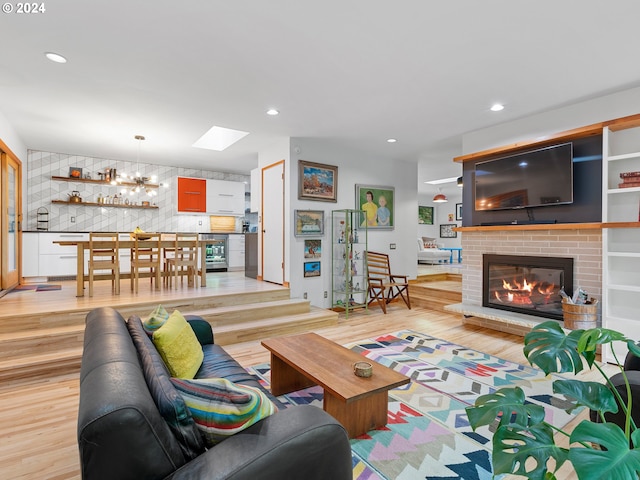 living room with a brick fireplace, a skylight, light hardwood / wood-style floors, and an inviting chandelier