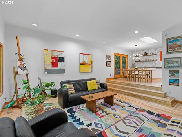 living room with a skylight, light wood-type flooring, and a chandelier