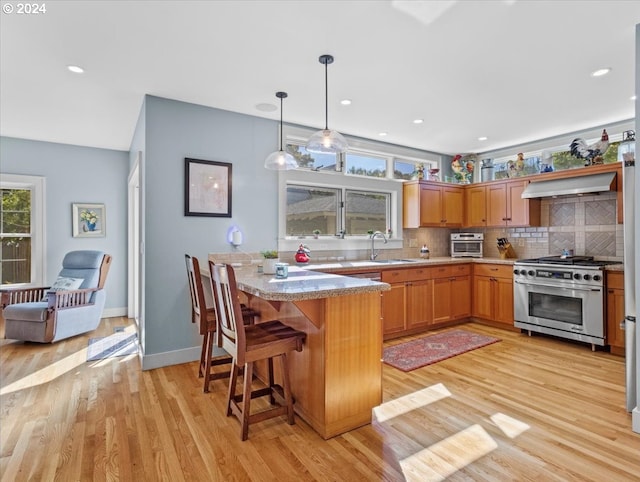 kitchen featuring pendant lighting, stainless steel range, kitchen peninsula, a breakfast bar, and light hardwood / wood-style floors