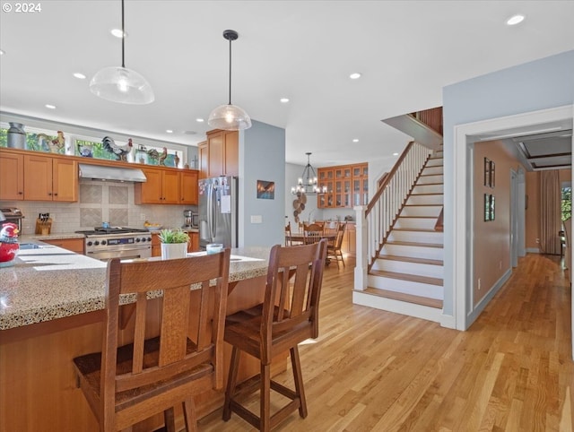 kitchen with light hardwood / wood-style flooring, pendant lighting, a notable chandelier, range hood, and appliances with stainless steel finishes