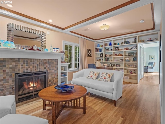 living room featuring a tiled fireplace, light hardwood / wood-style floors, and crown molding