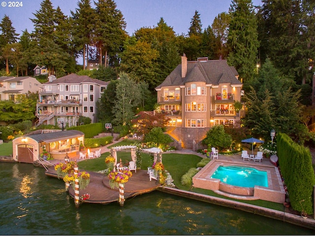 back of property featuring an outbuilding, a chimney, a water view, a patio area, and a balcony