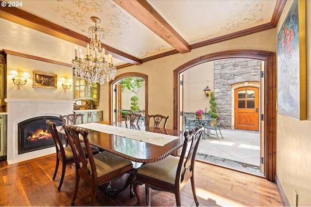 dining room with a fireplace with flush hearth, arched walkways, beam ceiling, and hardwood / wood-style floors