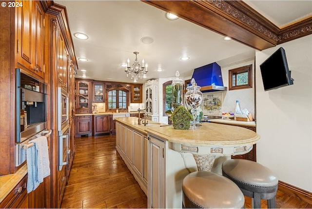 kitchen featuring brown cabinets, light countertops, glass insert cabinets, an island with sink, and a kitchen bar