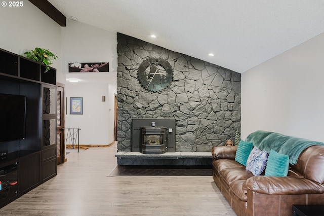 living area with baseboards, lofted ceiling, wood finished floors, a wood stove, and a textured ceiling