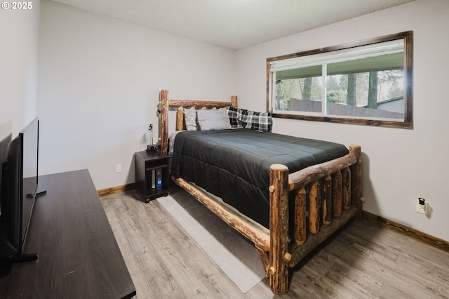 bedroom featuring light wood-style flooring, baseboards, and a textured ceiling