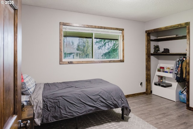 bedroom featuring a textured ceiling, a closet, wood finished floors, and baseboards