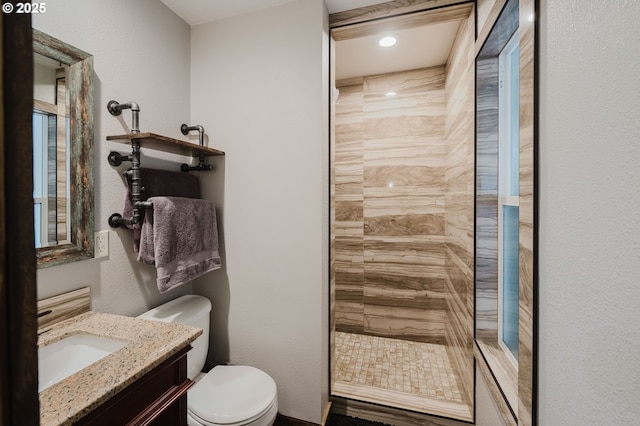 full bathroom with tiled shower, a textured wall, vanity, and toilet