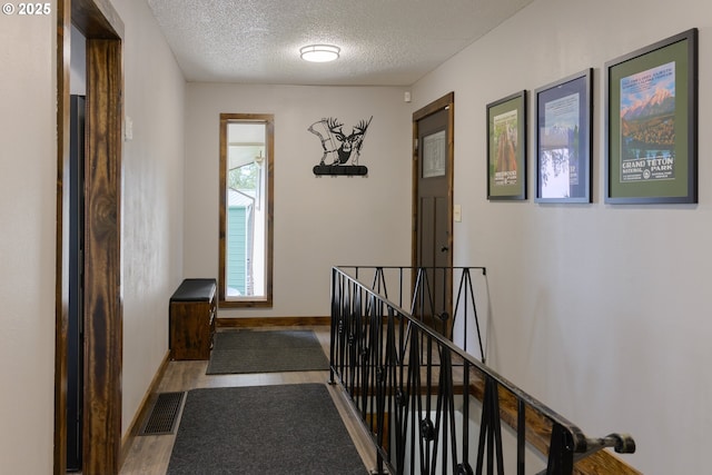 corridor with baseboards, visible vents, wood finished floors, a textured ceiling, and an upstairs landing