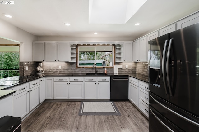 kitchen featuring open shelves, a sink, wood finished floors, black appliances, and dark countertops