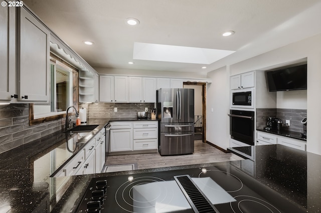 kitchen featuring a skylight, decorative backsplash, a sink, dark stone counters, and black appliances