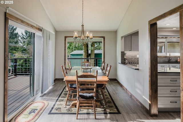 dining room featuring dark wood-type flooring, lofted ceiling, baseboards, and an inviting chandelier