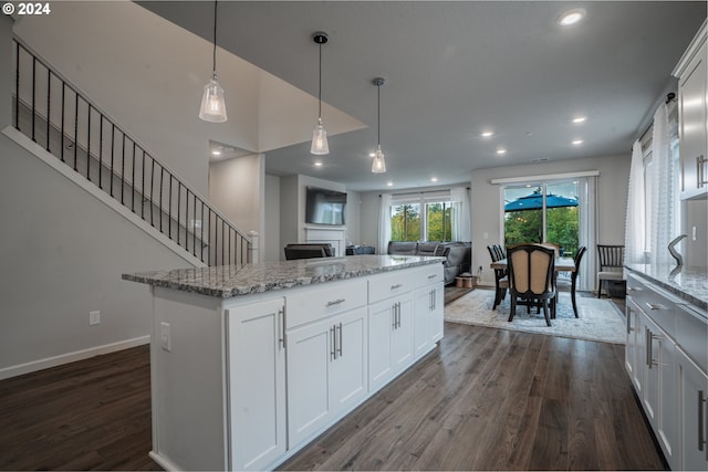 kitchen with decorative light fixtures, dark hardwood / wood-style flooring, a center island, light stone countertops, and white cabinets