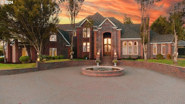 view of front facade with brick siding, curved driveway, and a lawn