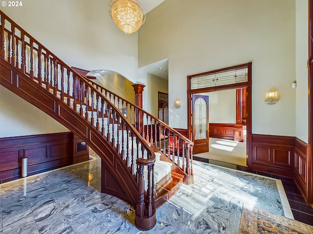 foyer entrance with arched walkways, stairway, a towering ceiling, an inviting chandelier, and wainscoting