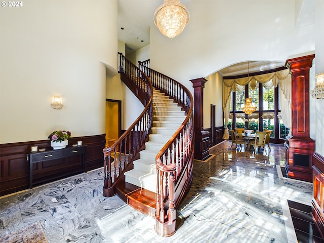 stairs with a towering ceiling, an inviting chandelier, a decorative wall, and wainscoting