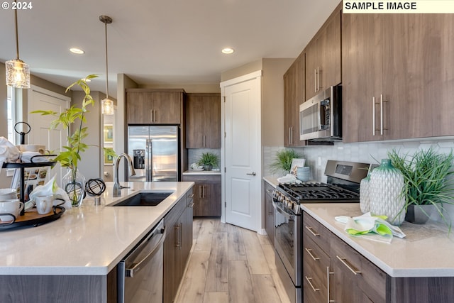 kitchen with pendant lighting, light hardwood / wood-style floors, backsplash, stainless steel appliances, and sink