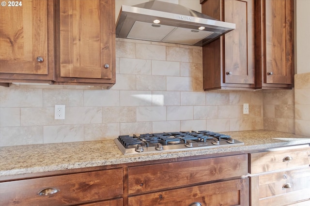 kitchen featuring stainless steel gas stovetop, decorative backsplash, light stone countertops, and wall chimney range hood