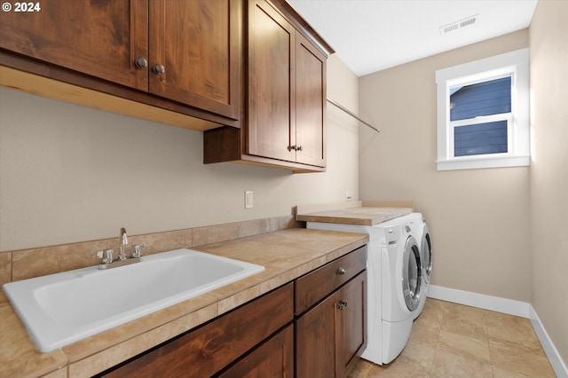 clothes washing area featuring cabinets, light tile patterned floors, washing machine and dryer, and sink