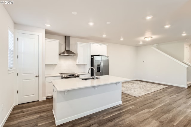 kitchen featuring stainless steel appliances, white cabinets, wall chimney exhaust hood, and an island with sink