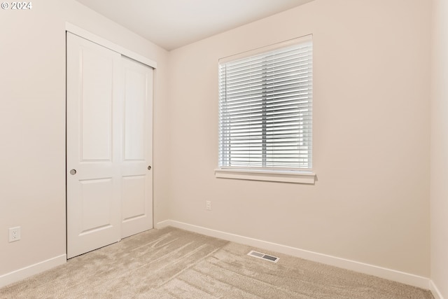 unfurnished bedroom with light colored carpet and a closet