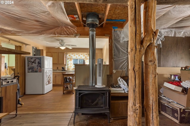 interior space with light wood-style flooring, a ceiling fan, freestanding refrigerator, light countertops, and a wood stove