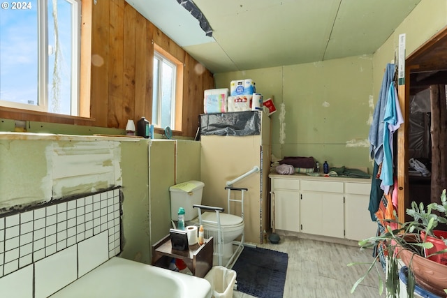 bathroom featuring a wealth of natural light, wood walls, toilet, and wood finished floors