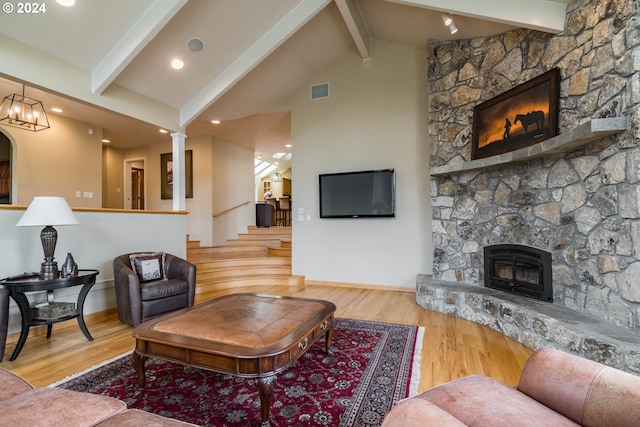 living area featuring a stone fireplace, wood finished floors, baseboards, stairs, and beamed ceiling