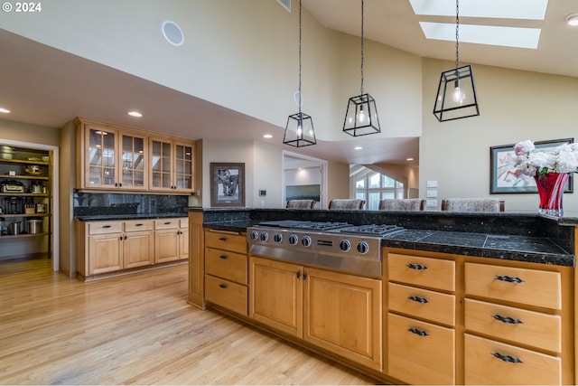 kitchen with light wood-style flooring, stainless steel gas cooktop, hanging light fixtures, tile counters, and glass insert cabinets