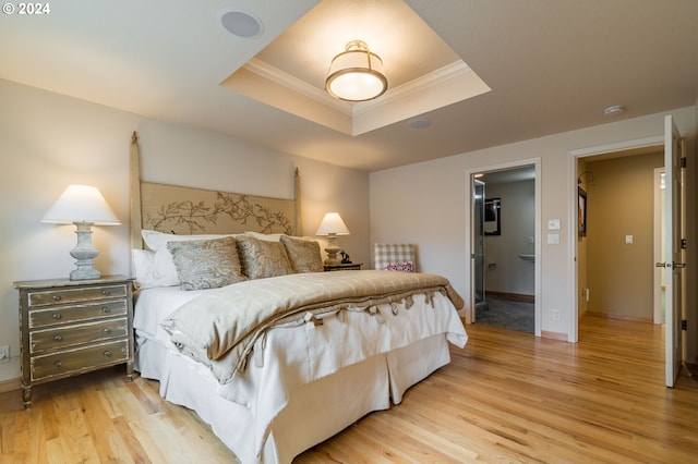 bedroom featuring light wood-type flooring, baseboards, a tray ceiling, and crown molding