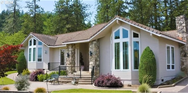 view of front of home featuring a patio, stone siding, a tile roof, a chimney, and crawl space