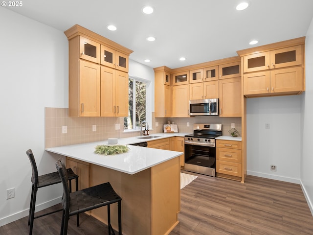 kitchen featuring hardwood / wood-style flooring, appliances with stainless steel finishes, tasteful backsplash, light brown cabinetry, and kitchen peninsula