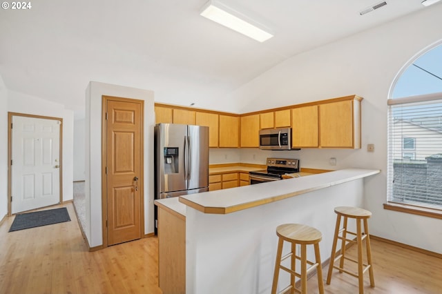 kitchen featuring light brown cabinets, kitchen peninsula, light hardwood / wood-style floors, vaulted ceiling, and appliances with stainless steel finishes