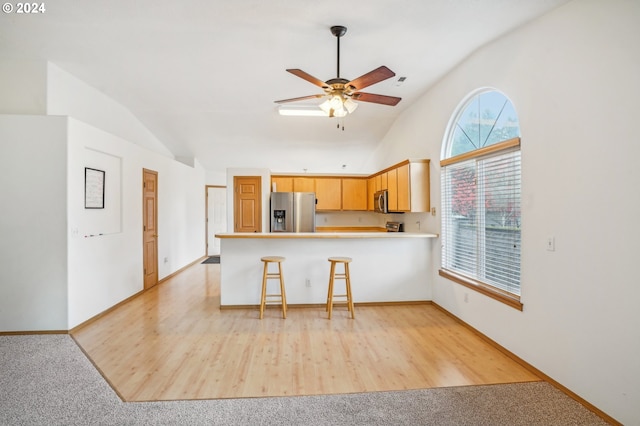 kitchen featuring kitchen peninsula, light brown cabinets, stainless steel appliances, and vaulted ceiling