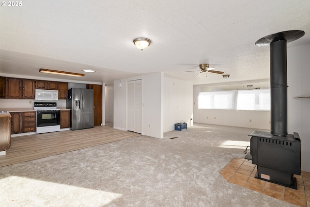 unfurnished living room featuring a wood stove, light carpet, and ceiling fan