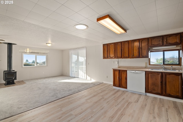 kitchen with light carpet, sink, a wood stove, and white dishwasher