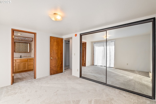 unfurnished bedroom with ensuite bathroom, sink, light colored carpet, and a closet