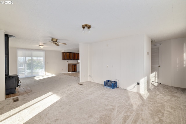 unfurnished living room featuring a wood stove, light carpet, and ceiling fan